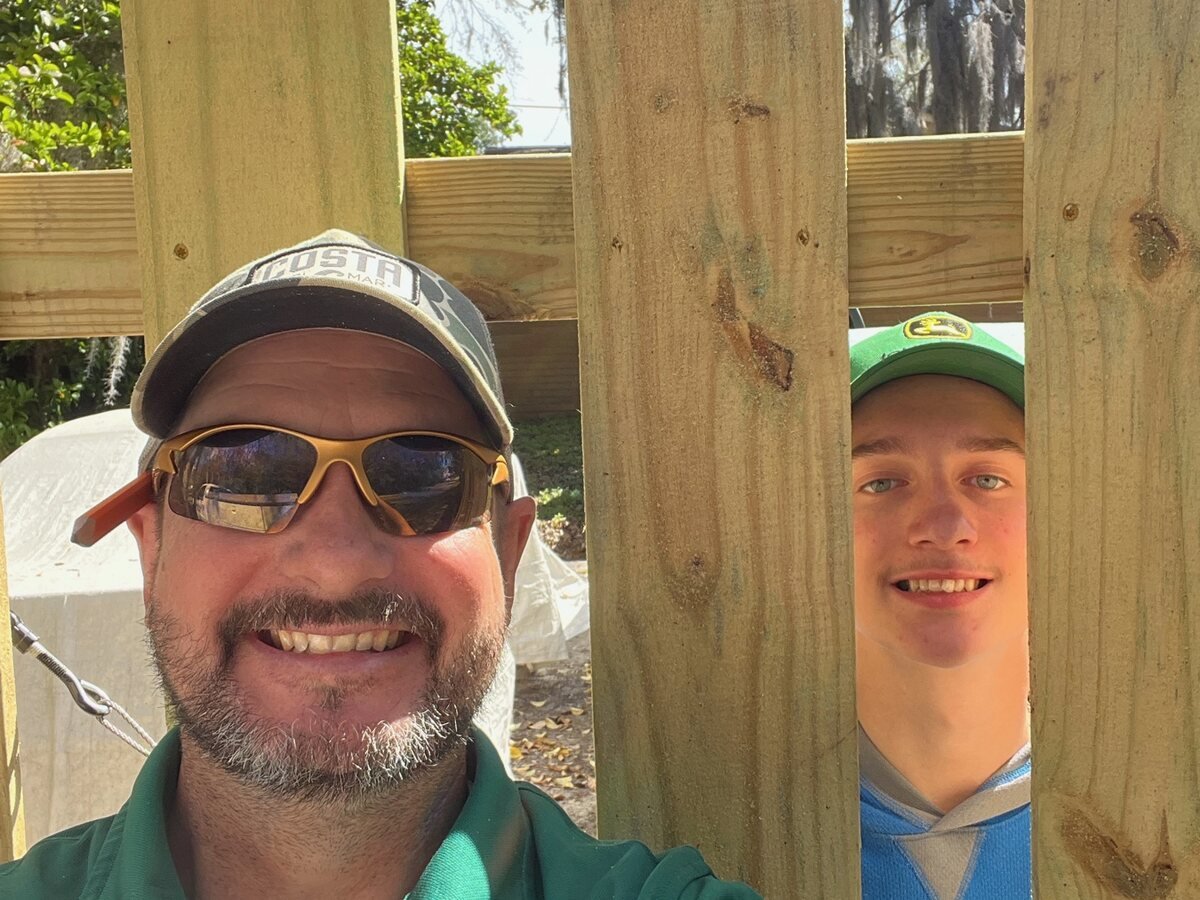 Tommy and one of his sons beside a wood fence under construction