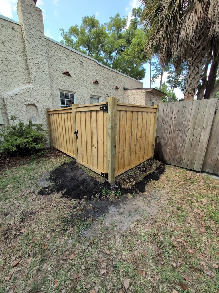 Corner view of a wood privacy fence and gate with a continuous horizontal top finish and flat-cut posts.