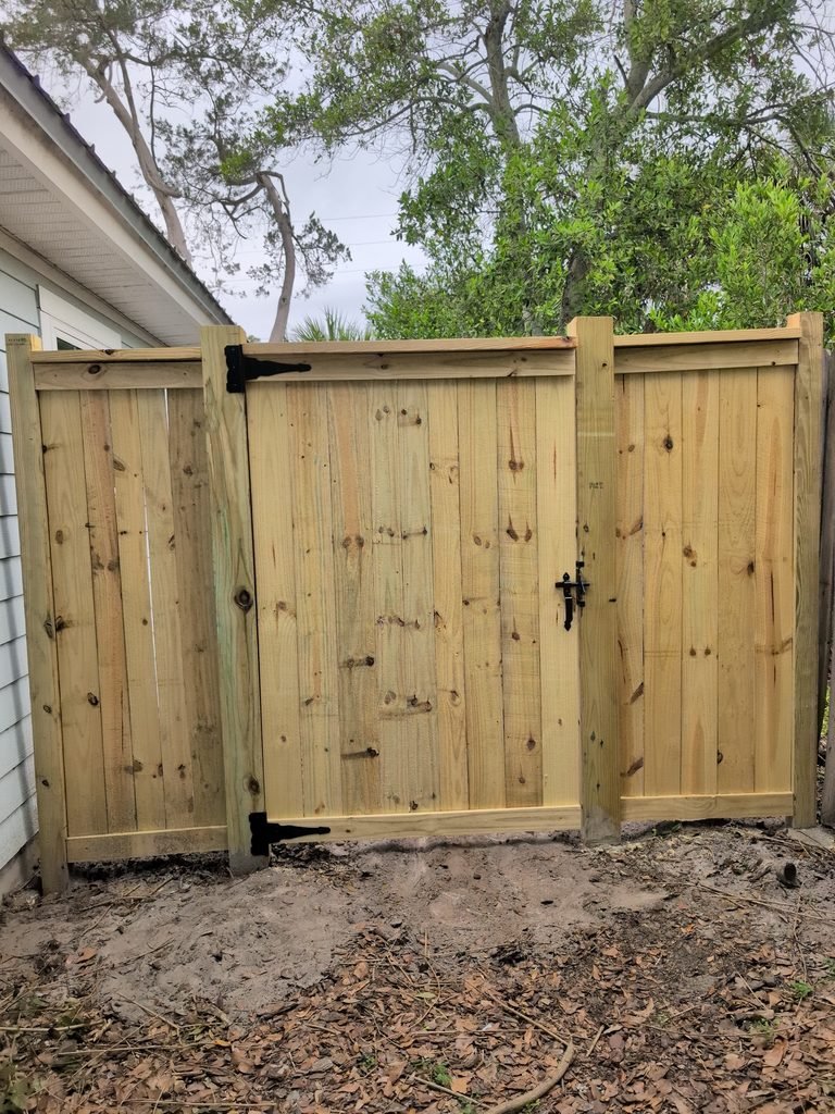 Close view of a wood privacy gate with black hinges and latch, horizontal trim, and uncapped flat-cut posts.